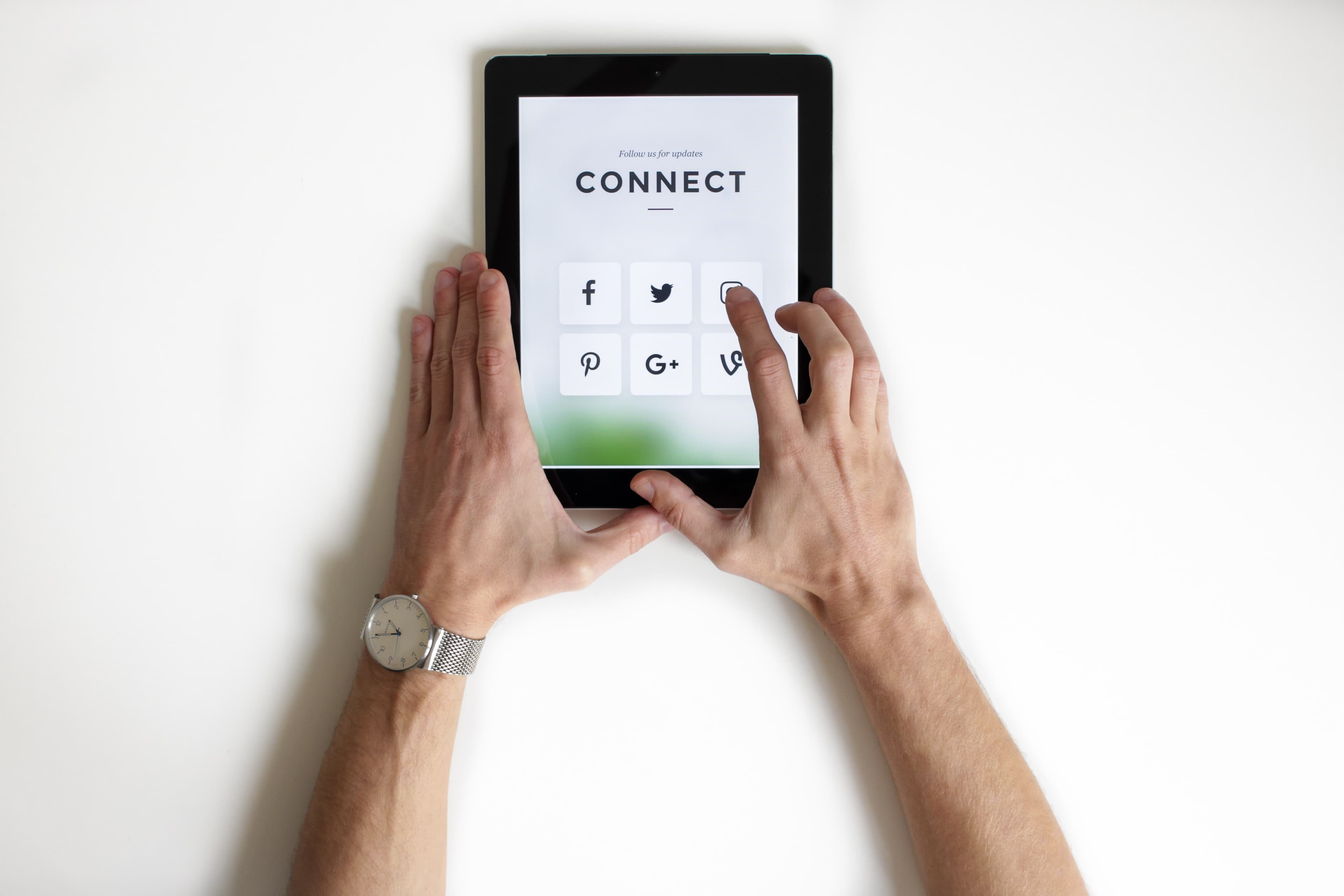 Overhead view of two hands holding a tablet showing a Connect screen with social media icons.