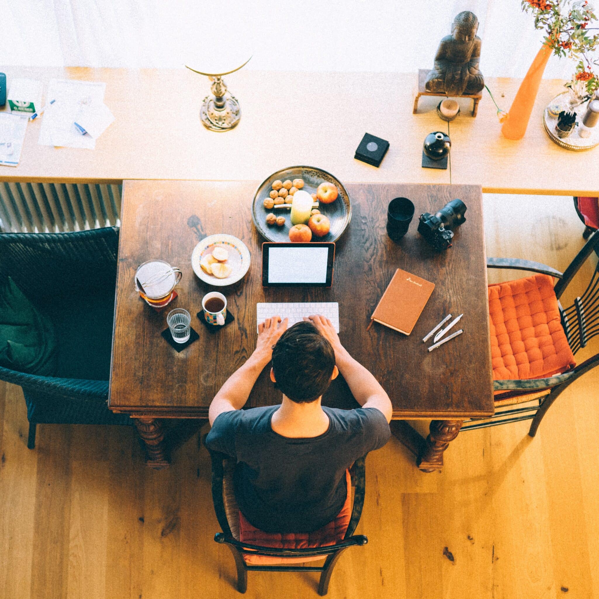 Overhead view of a man working at a tablet on a wooden dining table, with breakfast beside him.