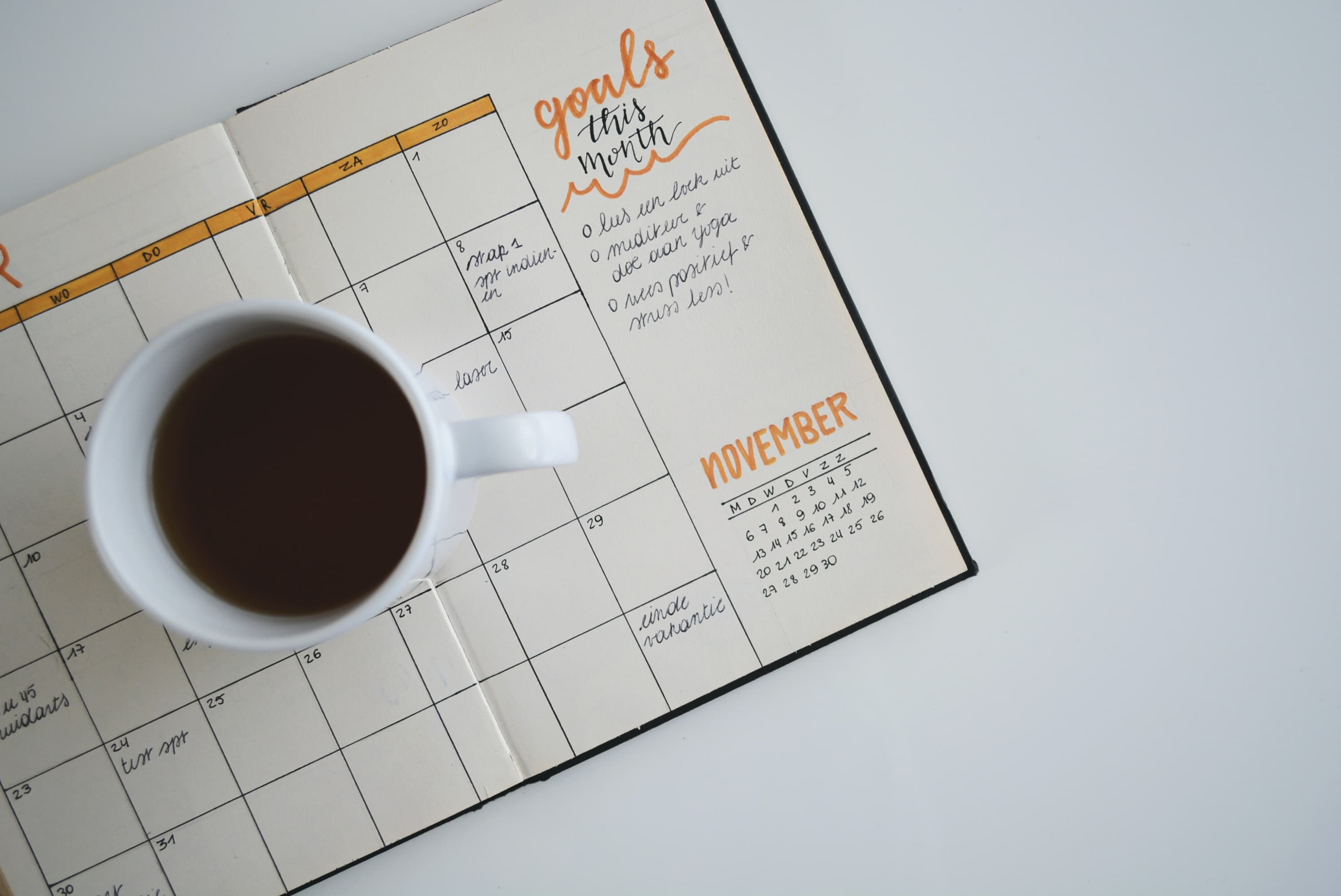 A cup of black coffee resting on an open monthly planner with goals written in the margin.