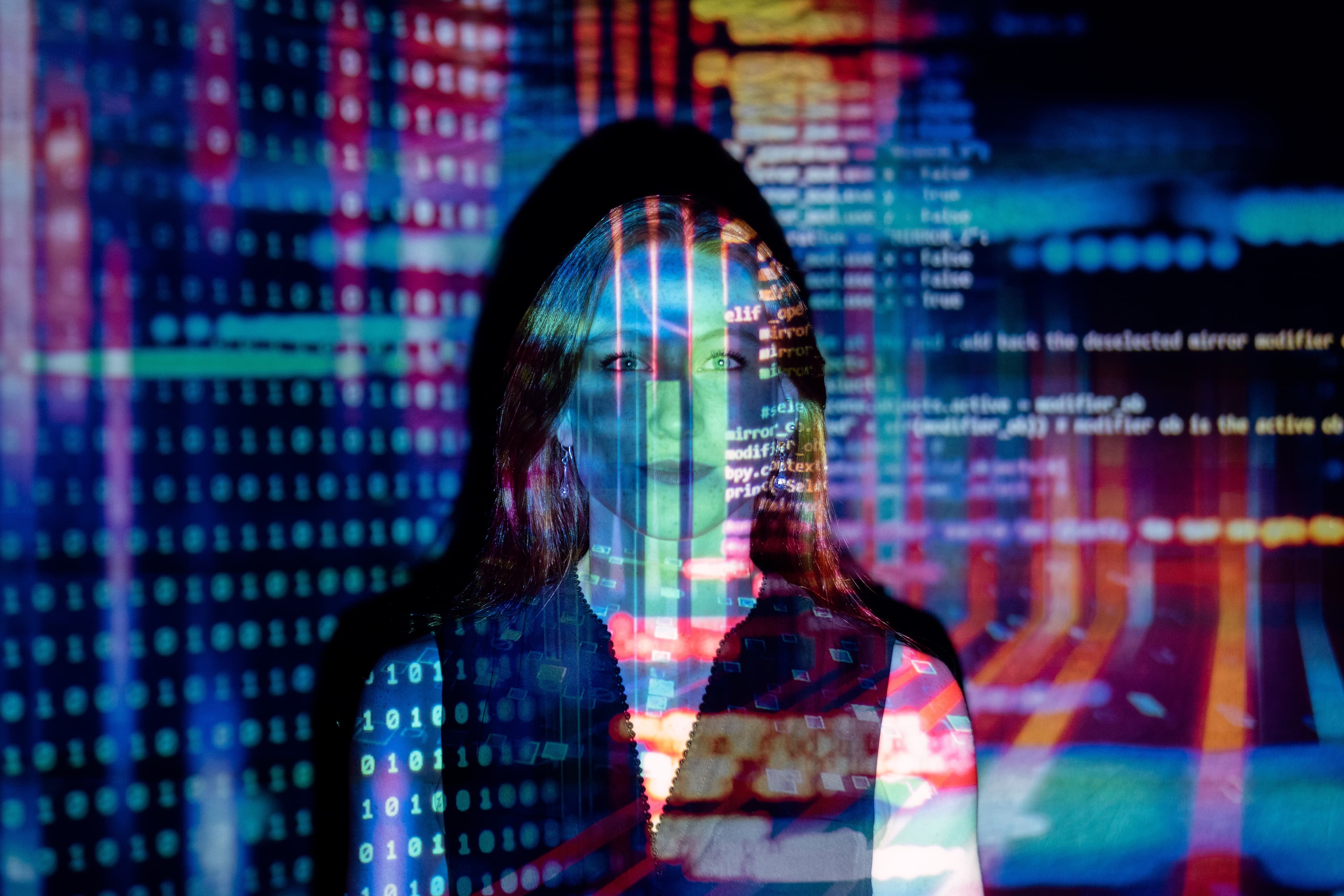 Image of a woman standing against a wall with colourful computer code projected over her